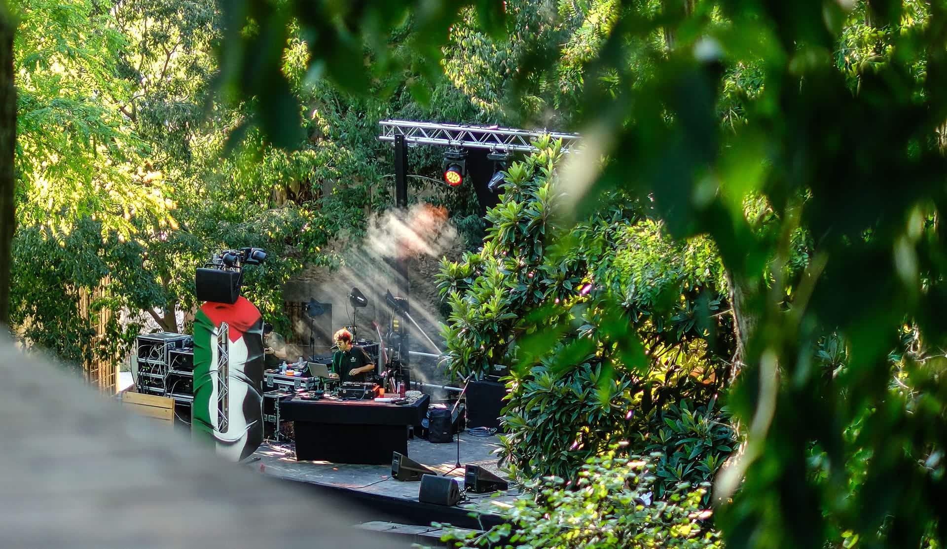 Montaje del equipo técnico y de sonido en un escenario ajardinado, entre árboles, durante la preparación de un concierto