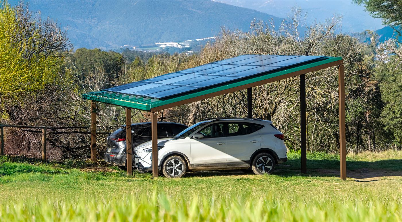 Estructura modular d'ombra productiva amb plaques solars instal·lada sobre dos cotxes, amb muntanyes al fons